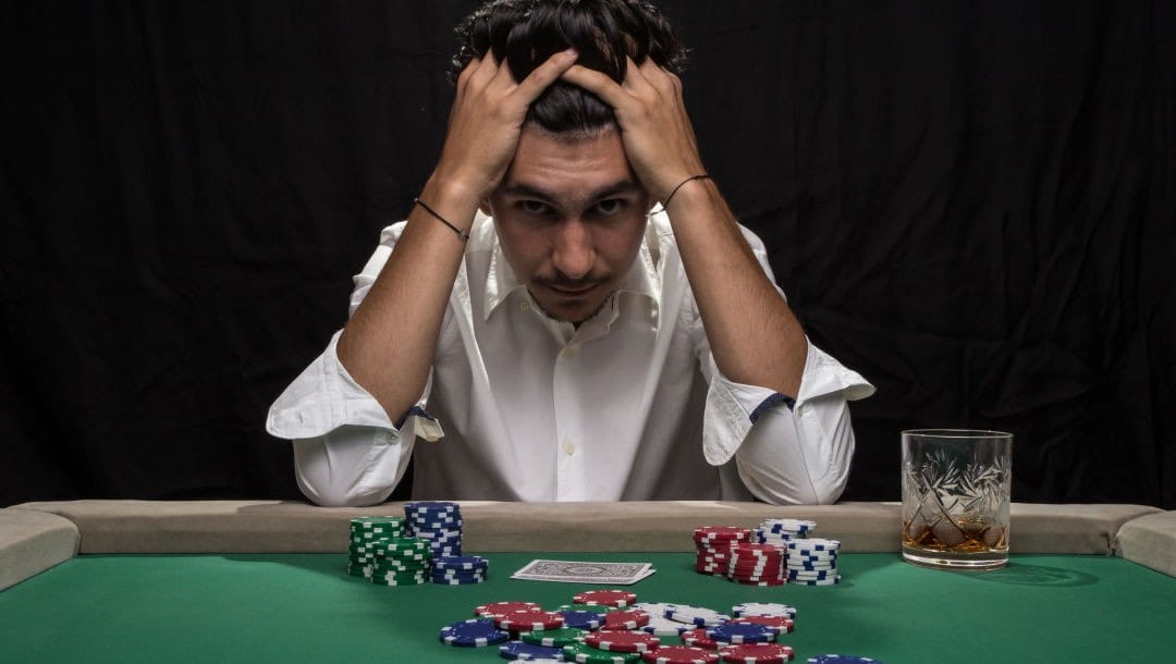 A man at a poker table with his head in his hands in frustration.