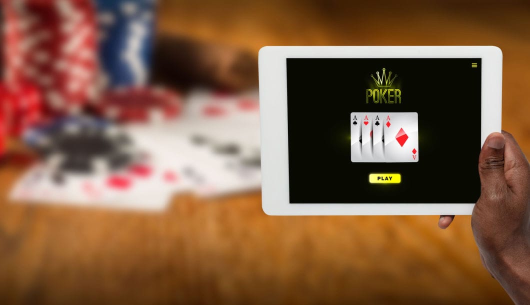 A hand holding a tablet featuring online poker with casino chips and cards in the background.