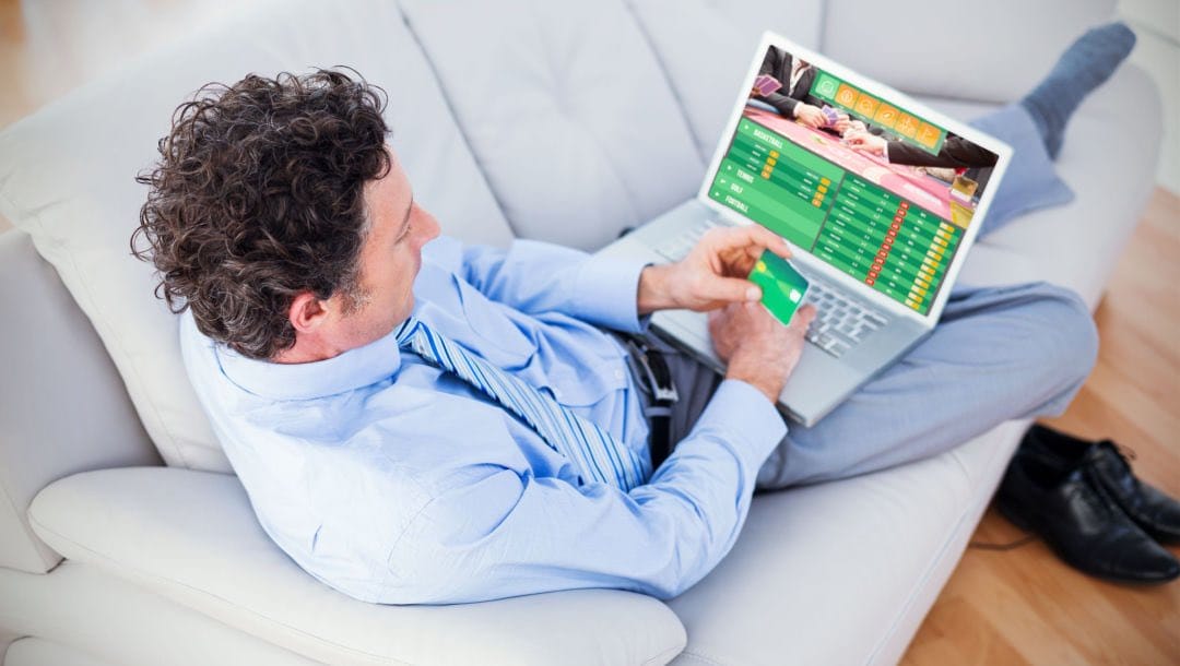 A man sitting on a couch playing poker on his laptop.