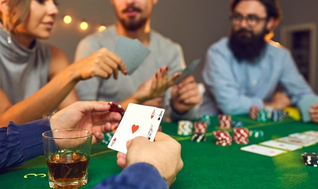 A group of friends sitting and playing poker around a table. One player holds a pair of aces and decides on his wager.