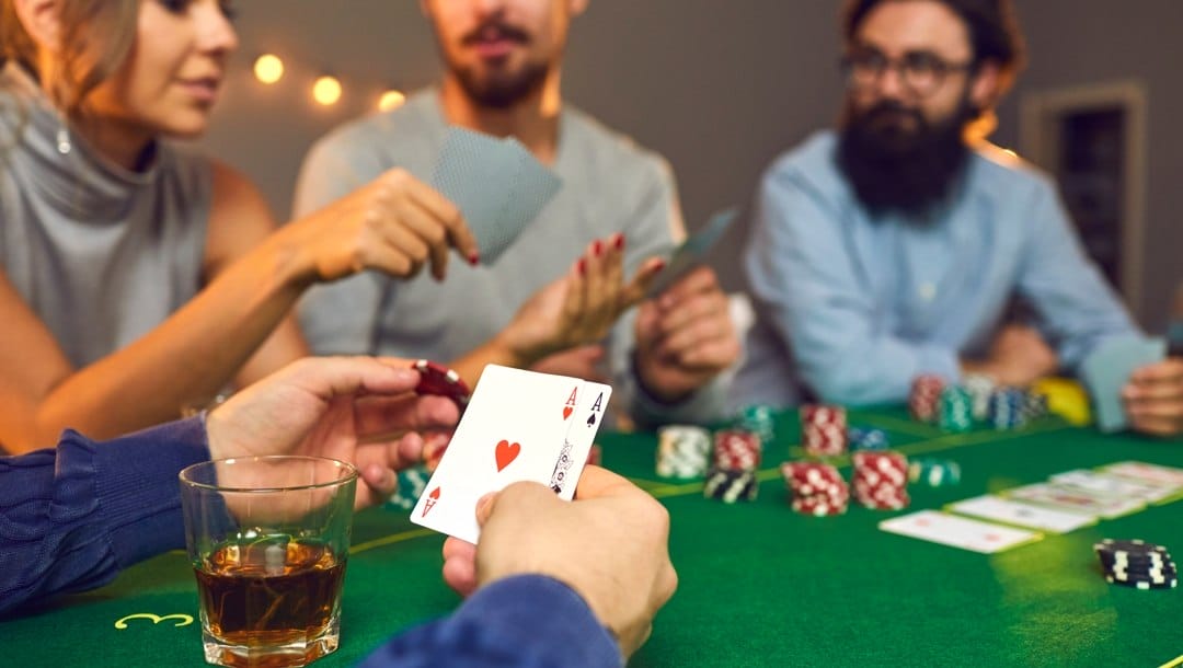 A group of friends sitting and playing poker around a table. One player holds a pair of aces and decides on his wager.