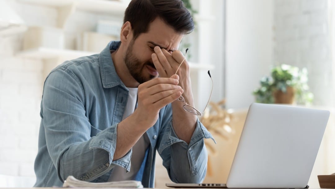 An exhausted man with eye strain in front of a laptop.