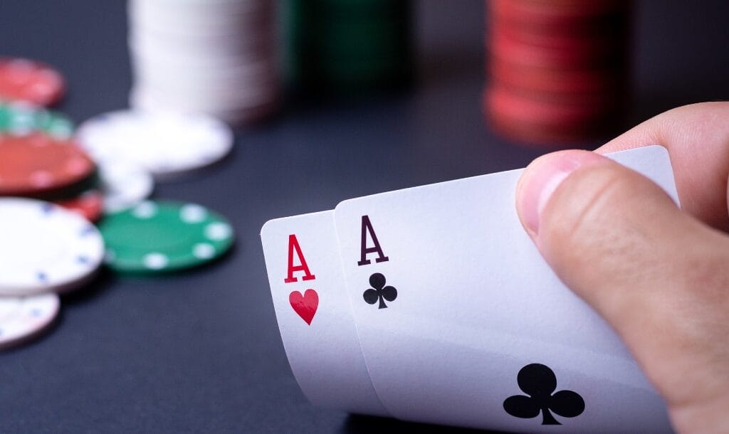 Ace poker cards held with two fingers and chips in the background.