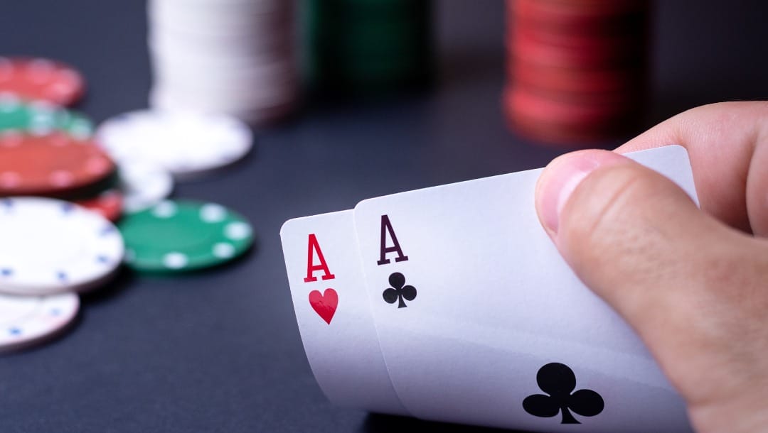 Ace poker cards held with two fingers and chips in the background.