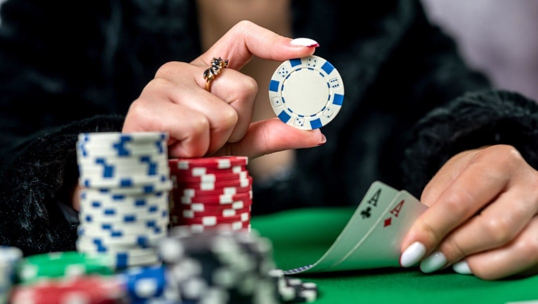 A woman holding two aces and a chip at a poker table.