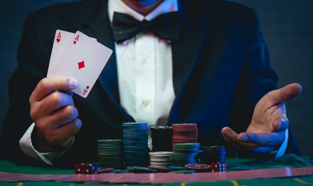 A man at a poker table with chips in front of him shows a pair of aces in his hand.