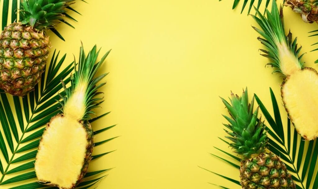 Pineapples and leaves on top of a yellow surface.