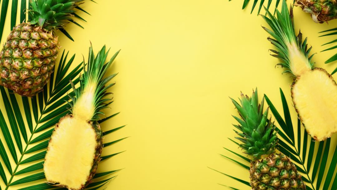Pineapples and leaves on top of a yellow surface.