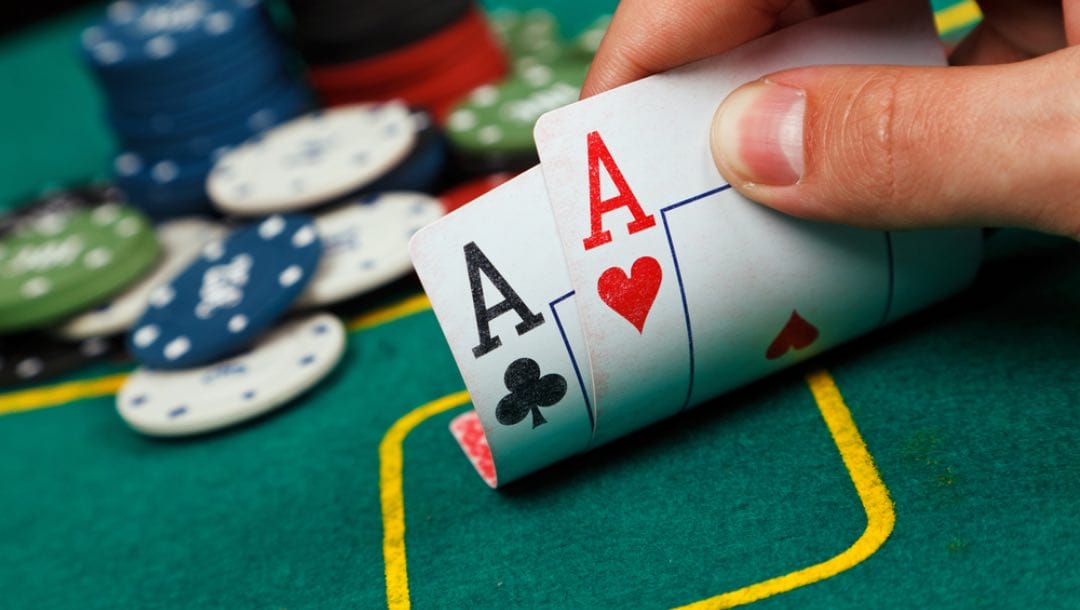 A person holds up two aces on a poker table with chips in the background.