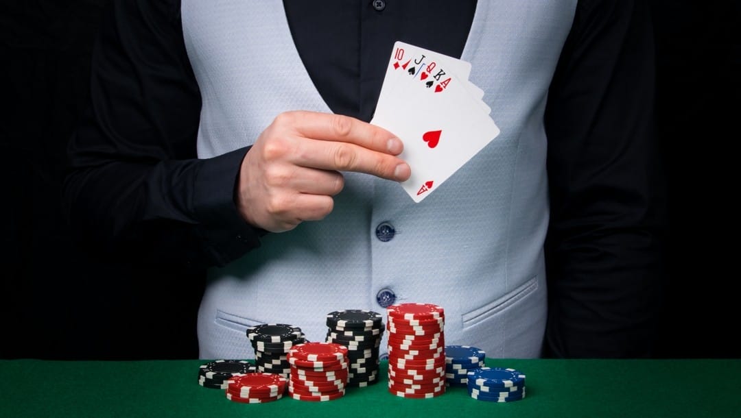 A player in a waistcoat stands in front of a poker table and reveals a straight in their hand.