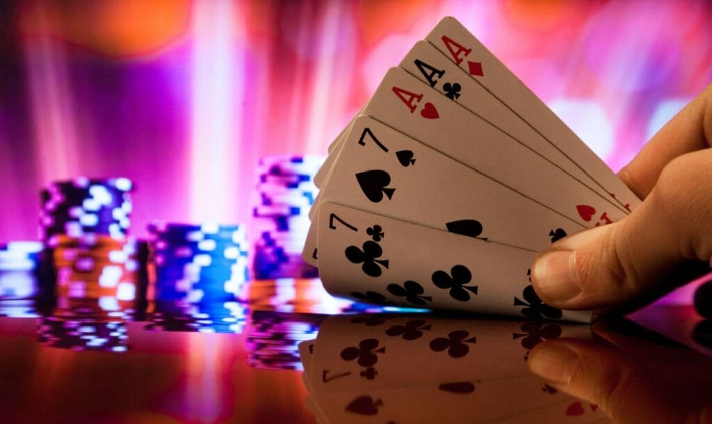 Hand holding poker cards featuring a full house. Neon lights and casino chips in the background.