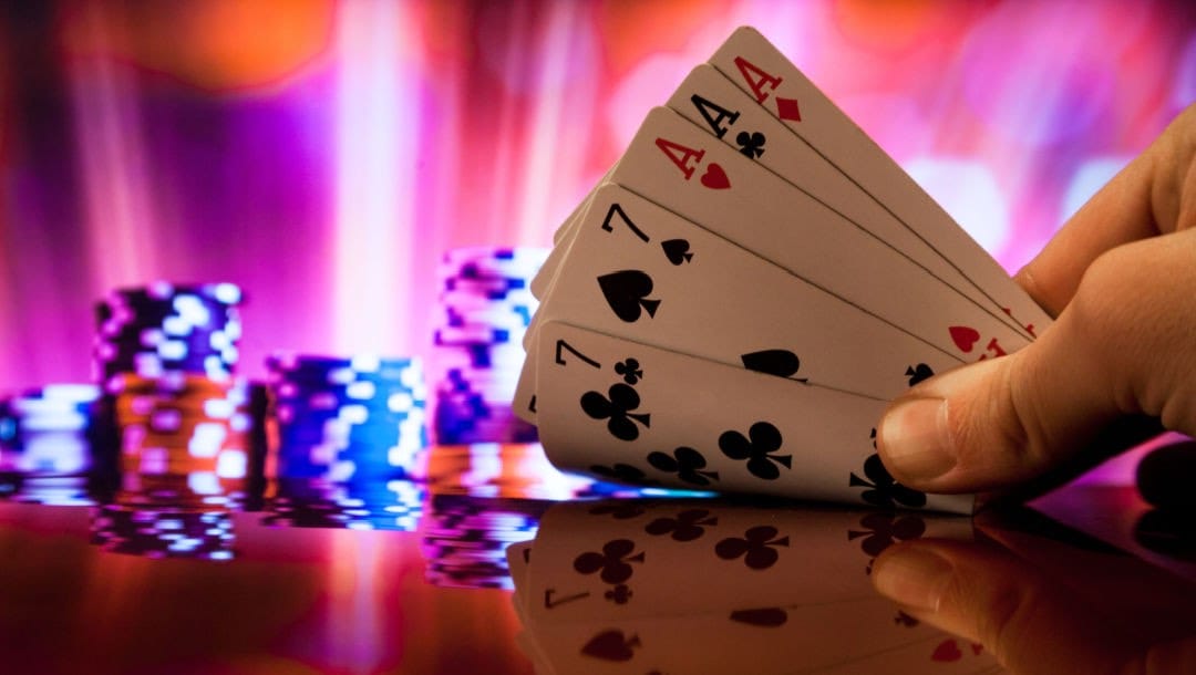 Hand holding poker cards featuring a full house. Neon lights and casino chips in the background.