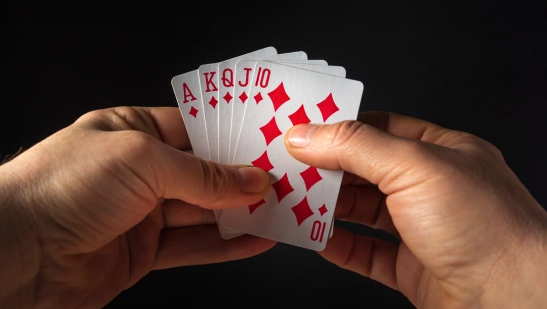 A person holding a straight poker hand up on a black background