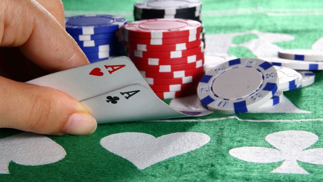 A poker player looks at their hole cards. There are poker chips behind their cards.