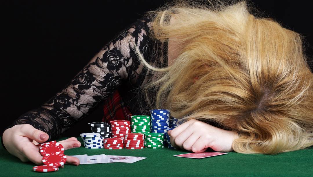 A woman with her head in her hands on a poker table drops her poker chips.