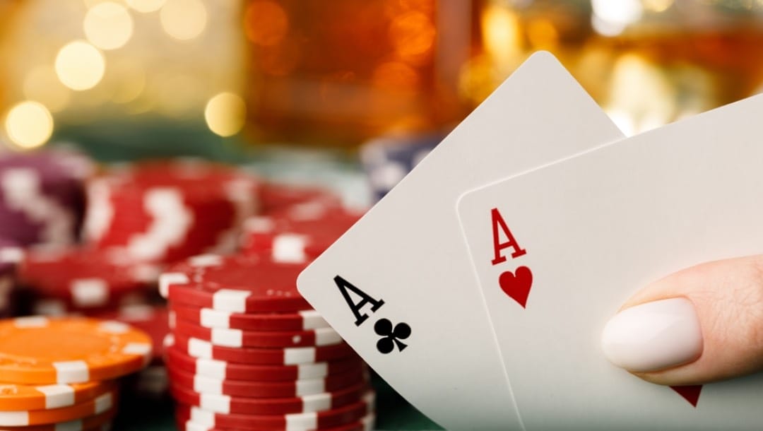 A person holding an ace pair with poker chips in the background.