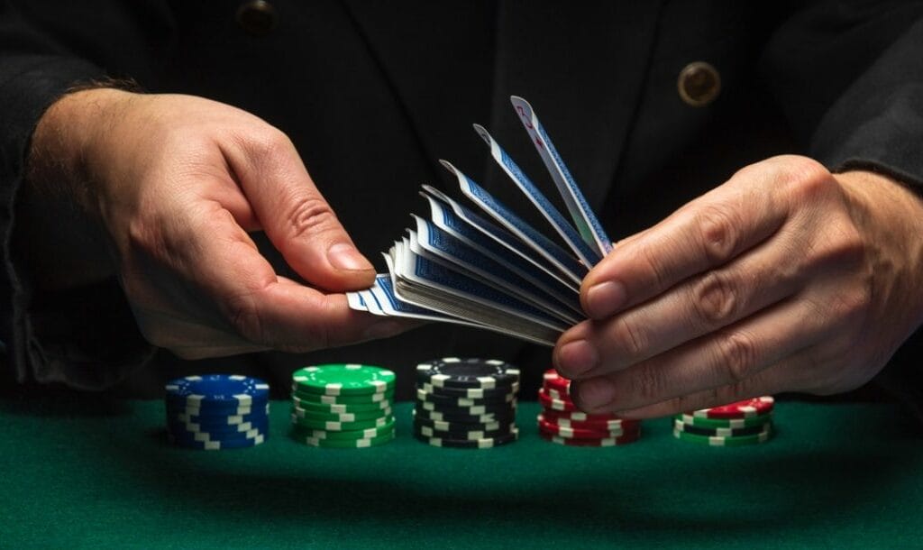 A dealer shuffling cards with poker chips beneath his hands.