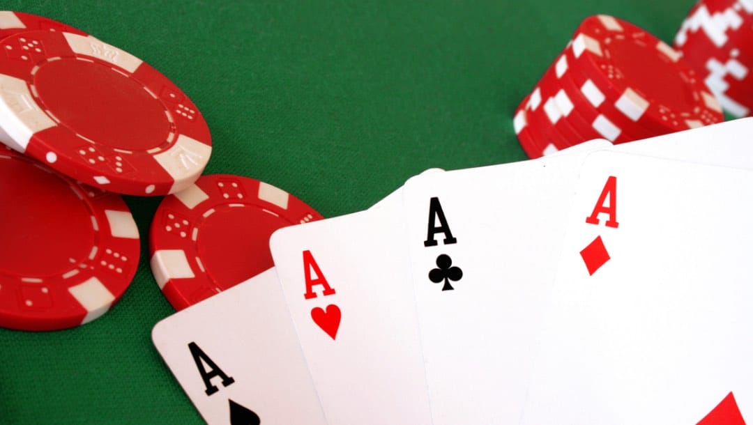 A hand with four aces on a poker table.