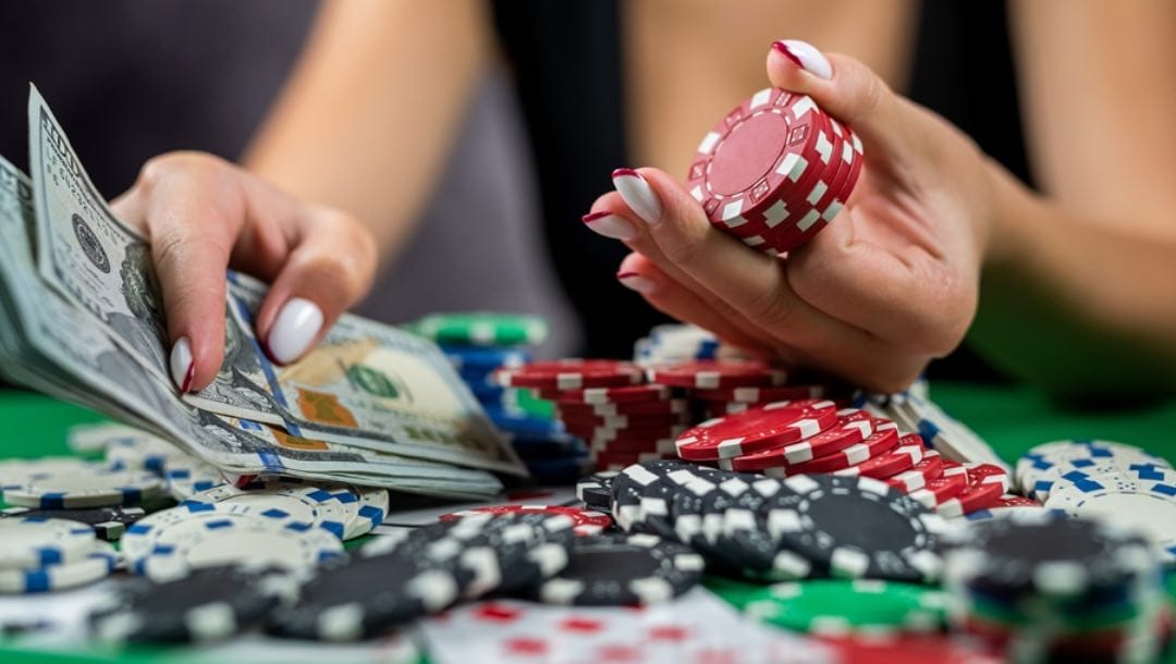 A woman holding cash and chips at a poker table.