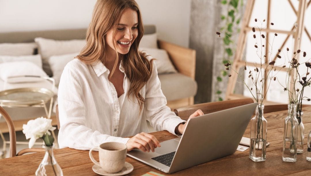 A woman sitting at a dining table playing online games on her laptop.