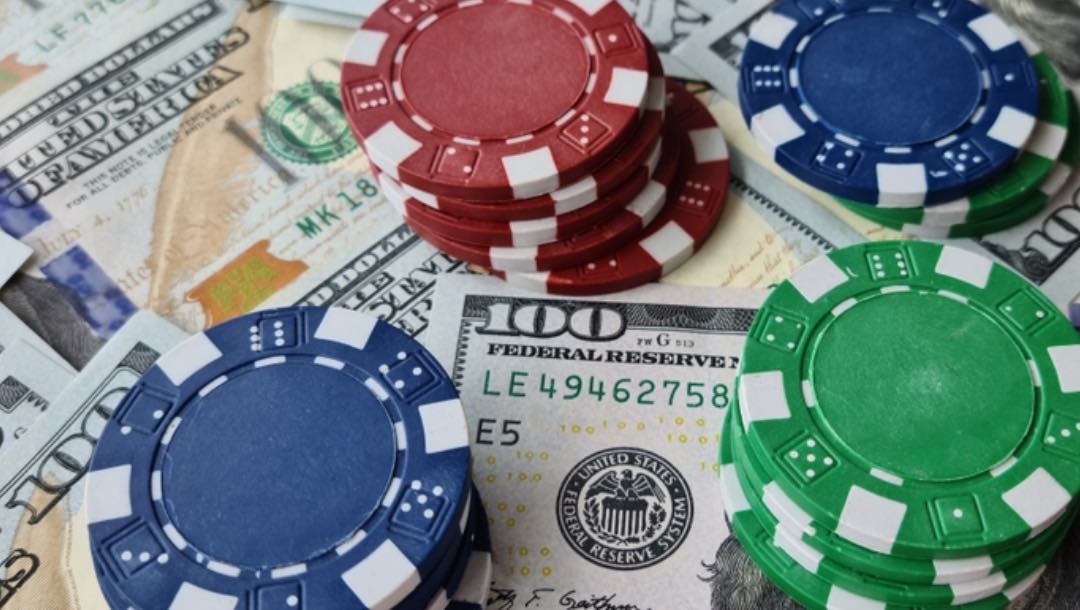 Small stacks of red, blue, and green poker chips on a background of $100 bills.