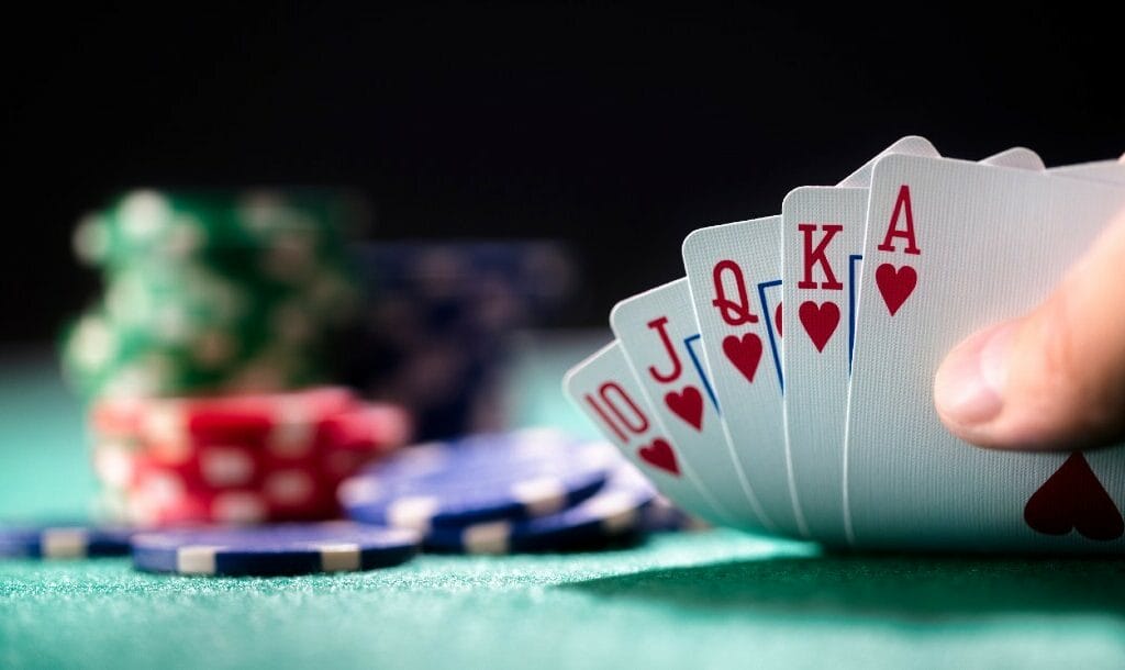 Hand holding a winning royal flush hand of cards with chips on the background