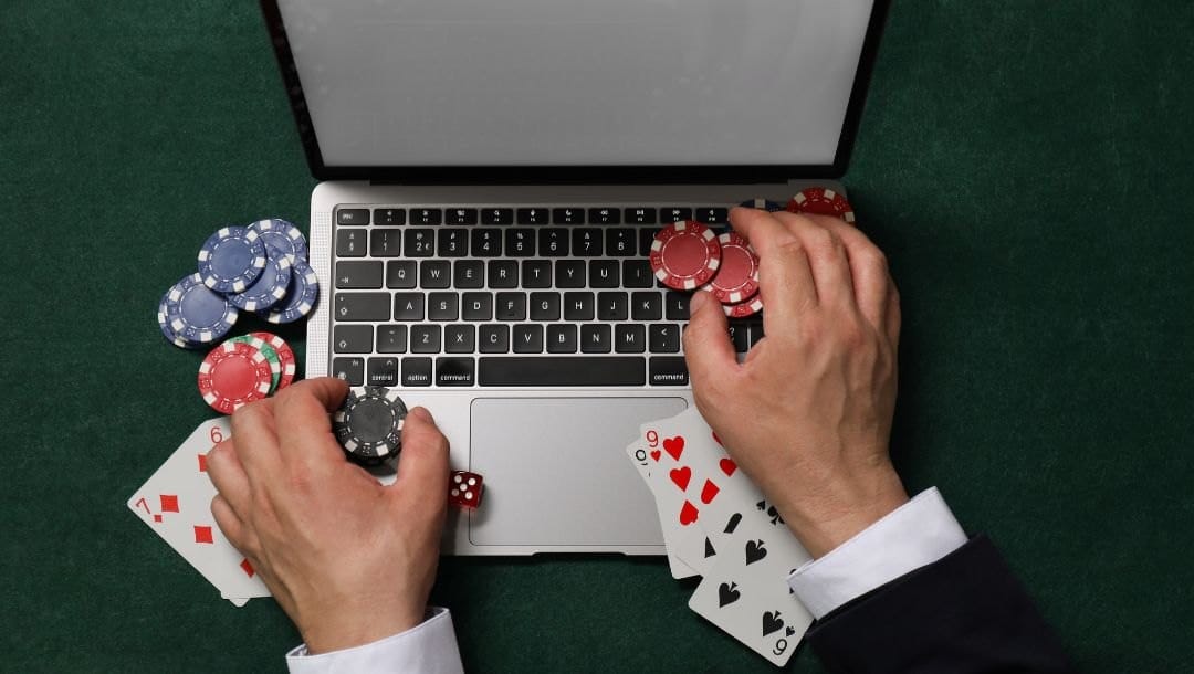 A person seated at a laptop computer, with playing cards and poker chips carefully arranged on the keyboard, blending virtual and physical elements of poker.
