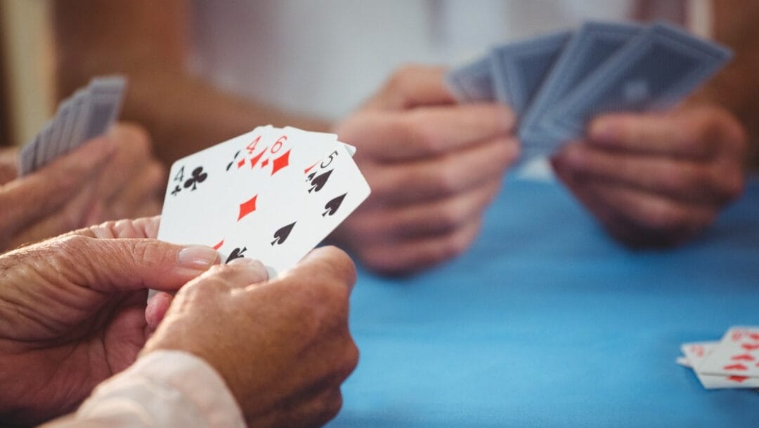 Three pairs of hands hold playing cards on a blue felt table