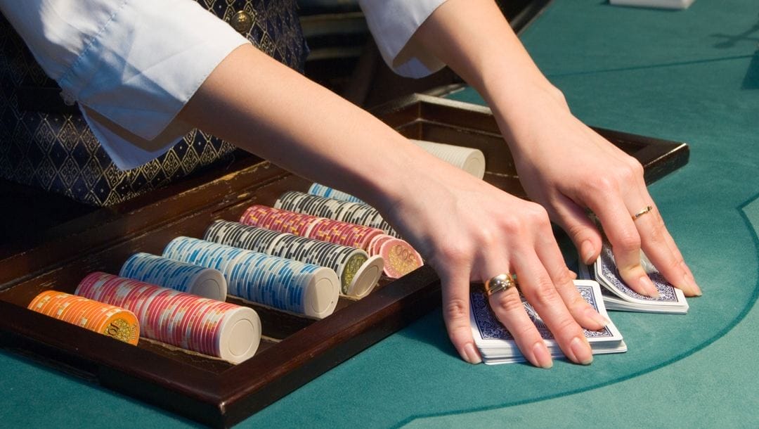A poker dealer shuffling a deck of cards. There is a tray filled with poker chips behind the cards.