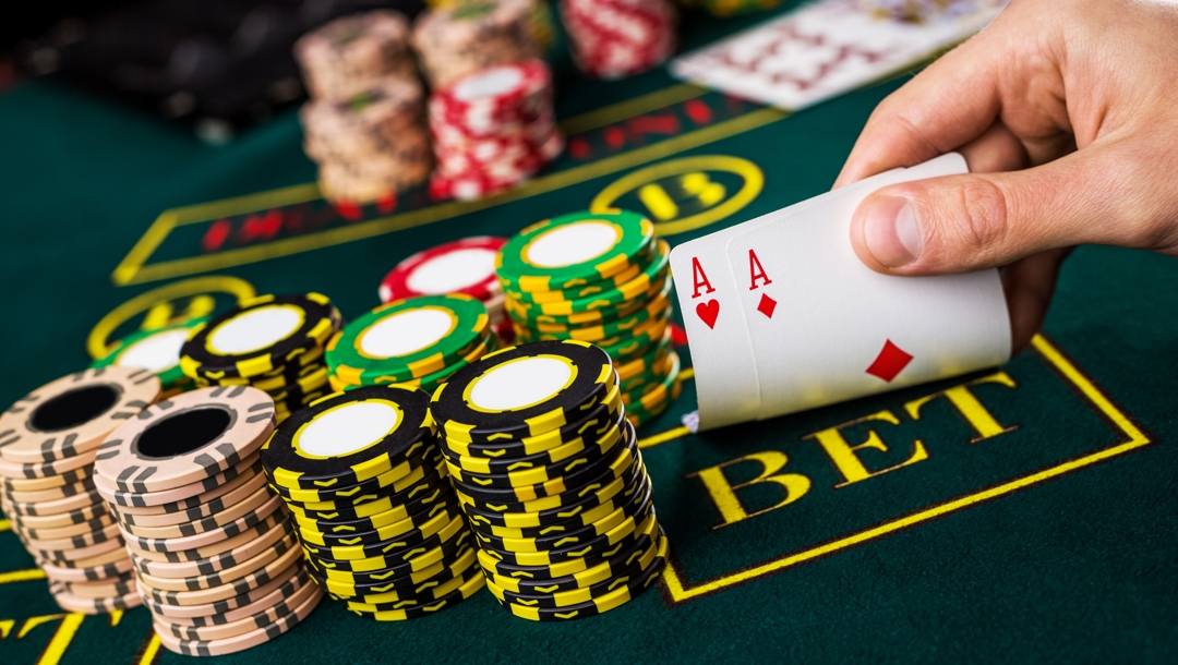A poker player checks their two hole cards during a game of Texas Hold’em. There are stacks of poker chips and community chips in the background.