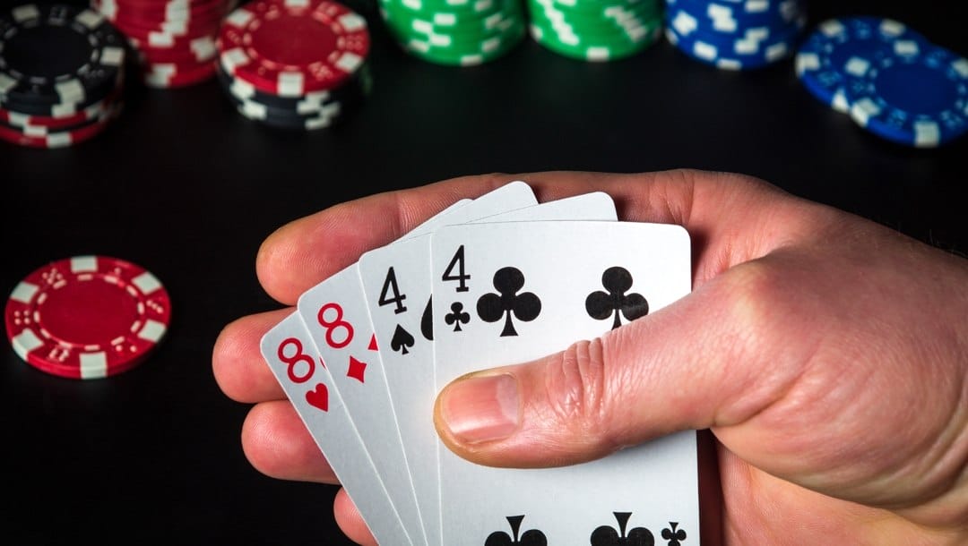 A poker player checks their four hole cards in a game of Omaha. There are stacks of poker chips in the background.