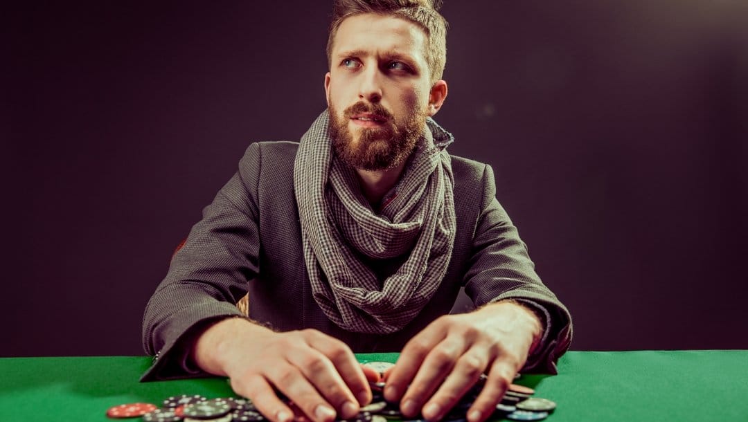 A man with his hands on a pile of poker chips looks up and to the right while thinking.