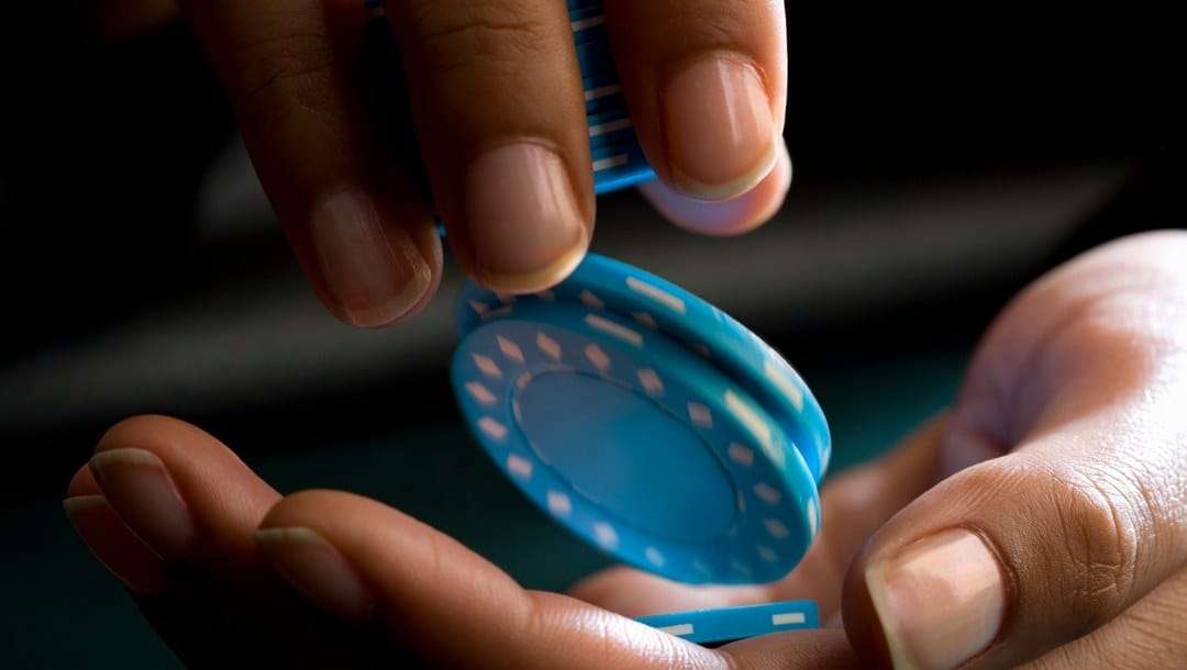 An extreme close-up of a poker player dropping blue poker chips from one hand into the other.
