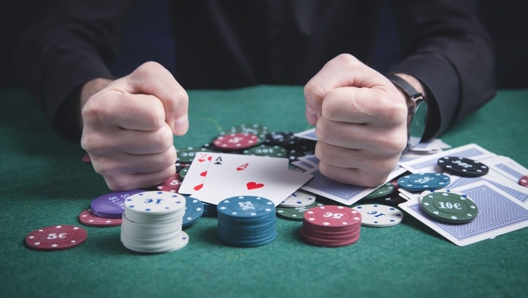 A man clenches his fists on top of playing cards and scattered poker chips.