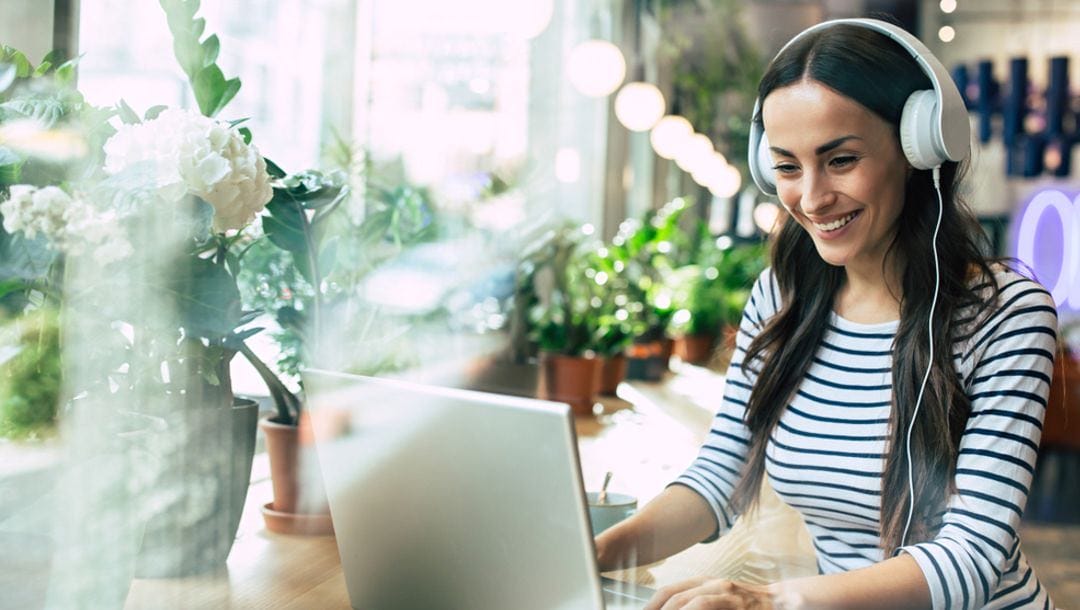 A woman in a café wearing headphones and working on her laptop.