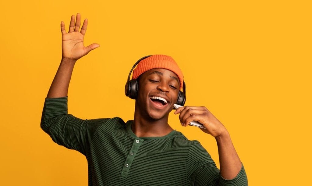 A man with headphones dances and sings against a bright yellow background.