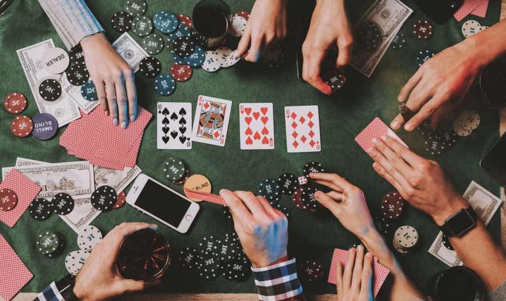 Aerial view of a group of friends’ hands touching cards and chips as they play poker.