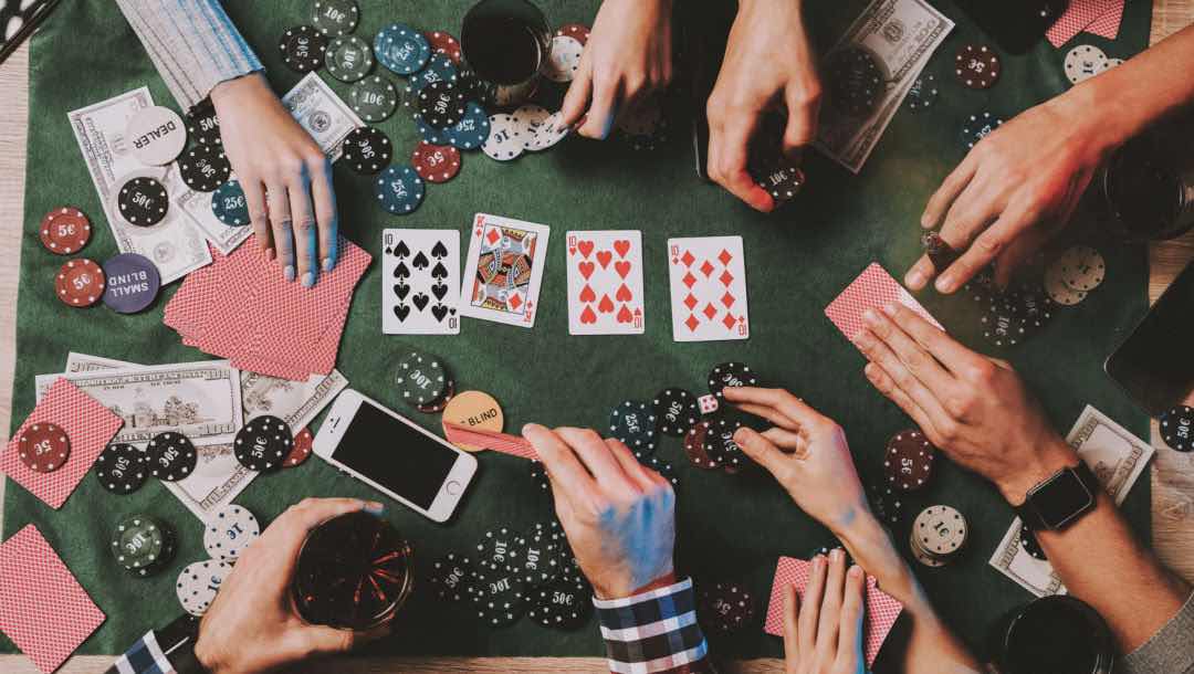 Aerial view of a group of friends’ hands touching cards and chips as they play poker.