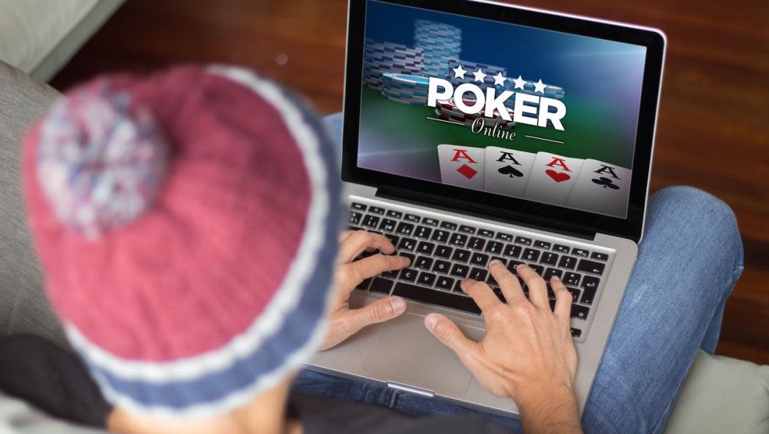 A man sitting on a couch playing online poker on a laptop.
