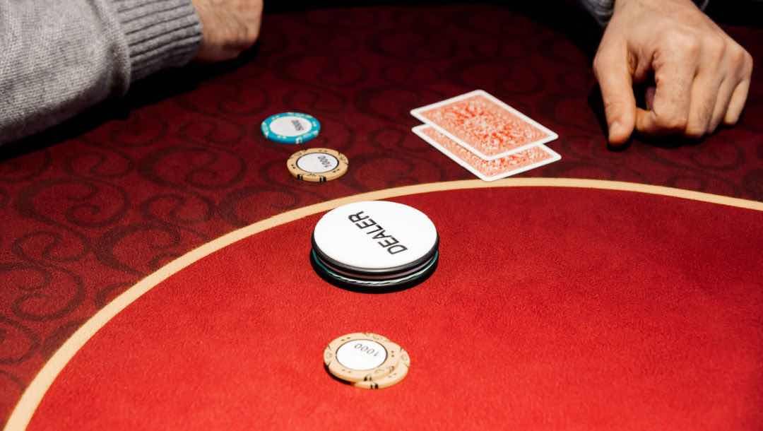 A person sitting at a poker table with the blind and dealer buttons in front of them