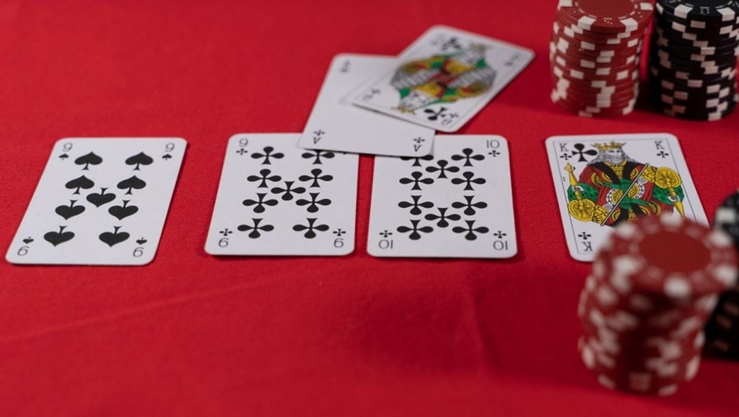 Playing cards spread out next to stacks of casino chips on a red poker table.