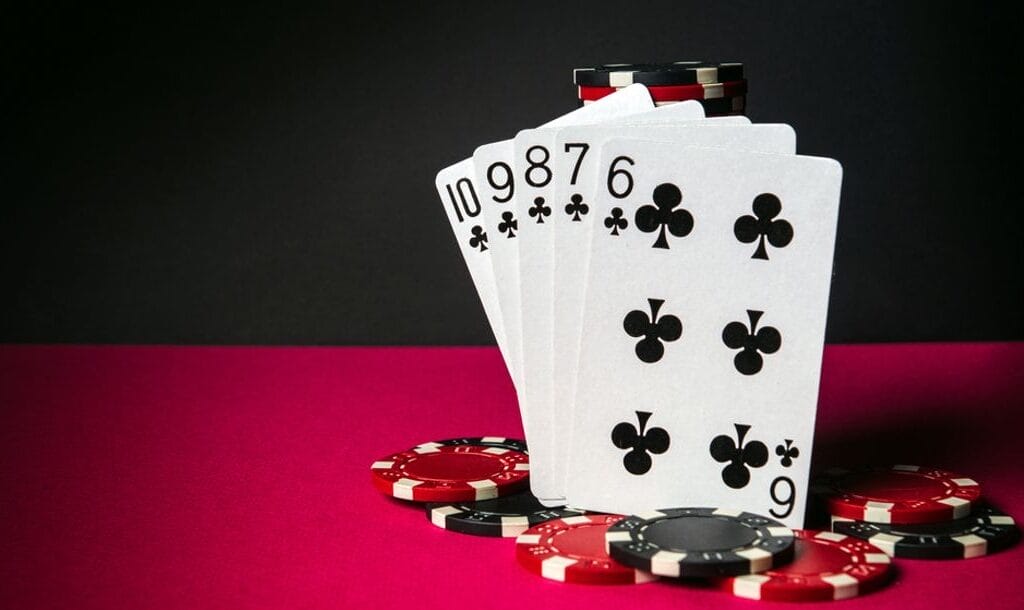 Playing cards featuring a straight flush surrounded by casino chips on a red poker table.