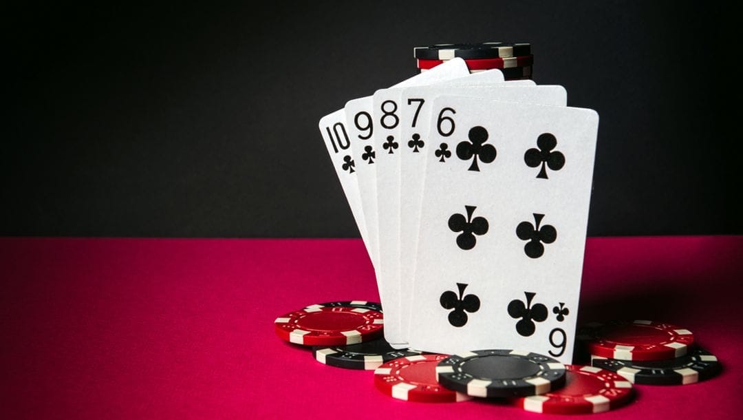 Playing cards featuring a straight flush surrounded by casino chips on a red poker table