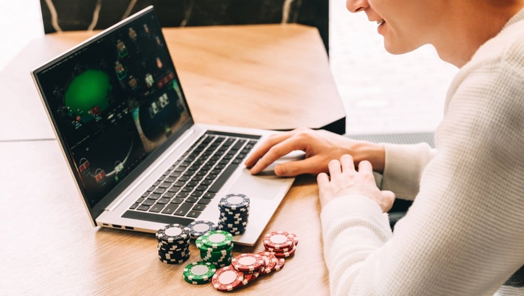 A man playing online poker on his laptop with poker chips on the table next to him.