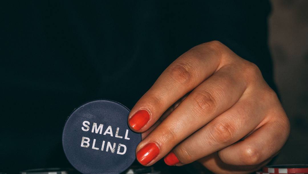 A player wearing red nail polish holds the small blind button.