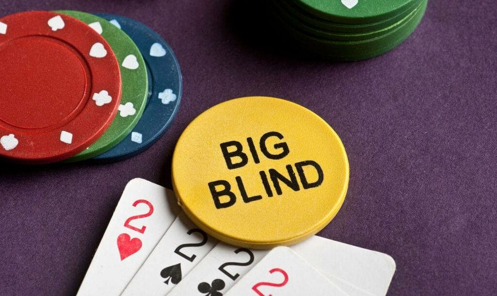 Four playing cards, a yellow big blind button and some poker chips on a poker table.