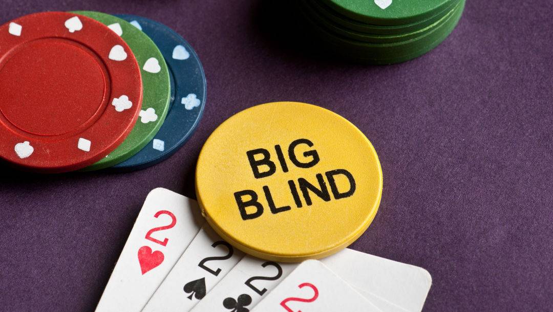 Four playing cards, a yellow big blind button and some poker chips on a poker table.