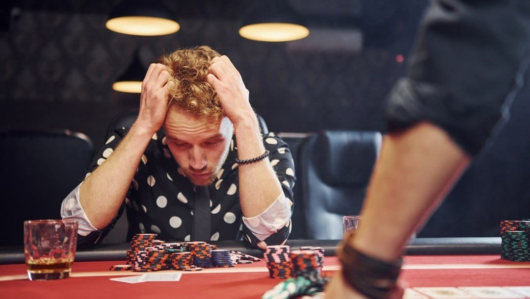 A poker player with their eyes closed and hands to their head after losing a round.