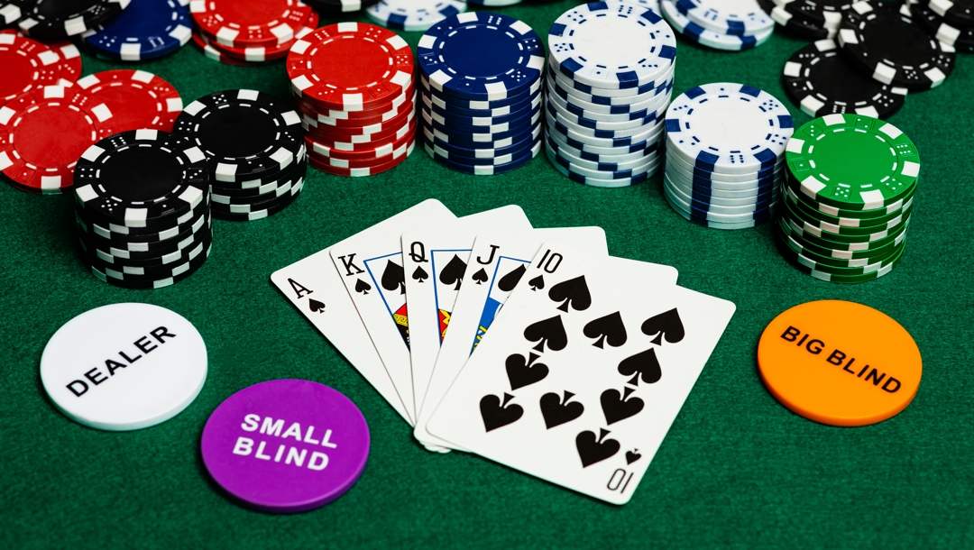 A small blind, big blind and dealer marker on a table next to a royal flush with stacks of poker chips behind them.