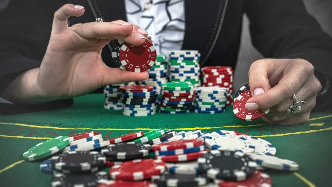 A woman raising bets in a poker game with casino chips in her hand.